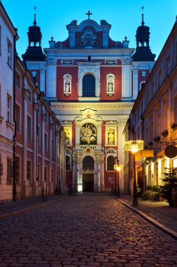 Poznan 'da akşam saatlerinde sütunlar ve heykellerle süslenmiş bir barok kilisesinin cephesi.