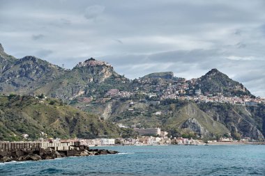 İtalya 'nın Sicilya adasındaki Naxos' ta, dağlık alanda beton bir dalgakıranı ve binaları olan deniz kıyısı.