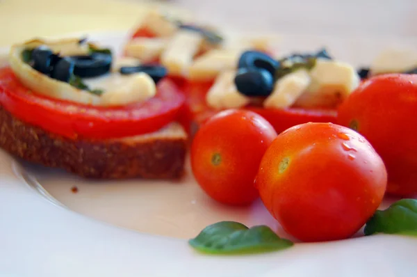 Bruschetta dengan tomat, zaitun hitam, keju kambing, rempah-rempah dan minyak pada roti panggang — Stok Foto