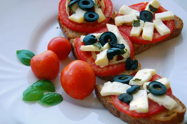 Bruschetta com tomate, azeitonas pretas, queijo de cabra, ervas e óleo sobre pão torrado — Fotografia de Stock