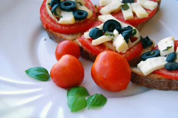 Брускетта з помідорами, чорними оливками, козячим сиром, травами та олією на підсмаженому хлібі — стокове фото