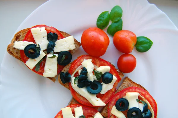 Bruschetta com tomate, azeitonas pretas, queijo de cabra, ervas e óleo sobre pão torrado — Fotografia de Stock