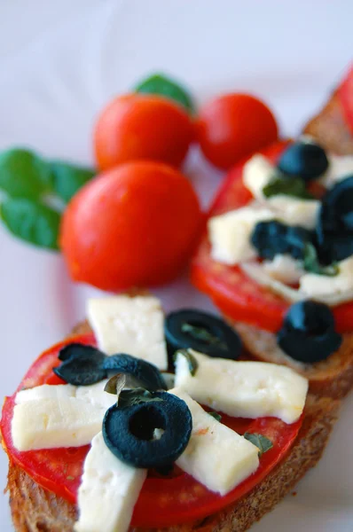 Брускетта с помидорами, черными оливками, козий сыр, травы и масло на поджаренном хлебе — стоковое фото