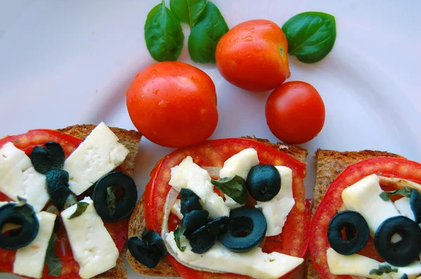 Bruschetta dengan tomat, zaitun hitam, keju kambing, rempah-rempah dan minyak pada roti panggang — Stok Foto