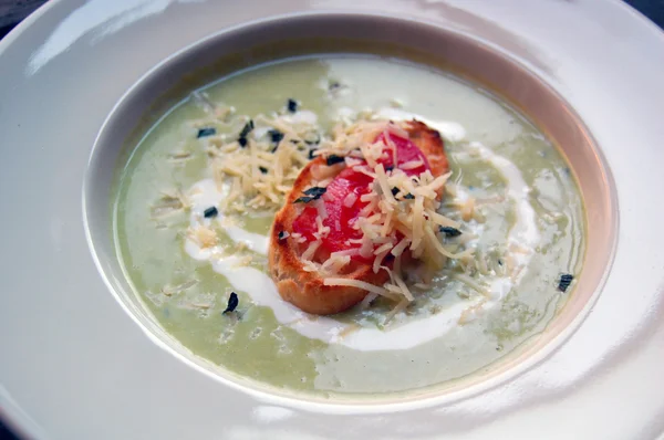 Close up of green pea soup with bread and cheese on top — Stock Photo, Image