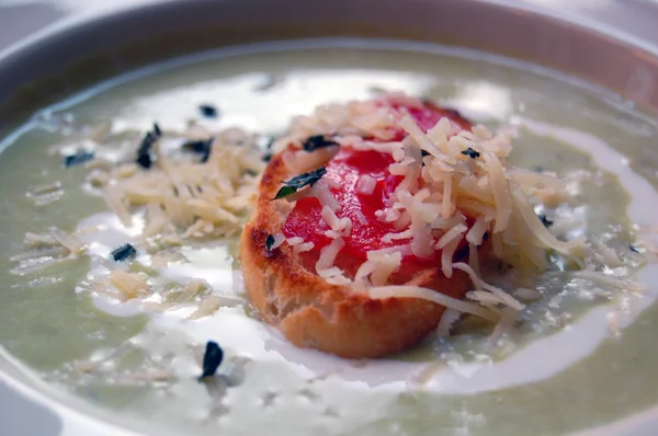 Close up of green pea soup with bread and cheese on top — Stock Photo, Image