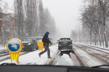Kyiv, Ukrayna, 23 Aralık 2020, şiddetli kar yağışı ve aşırı kötü hava koşullarında bir köpek ile karşıya geçen yaya.