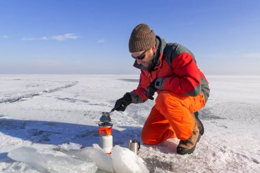 Portatif gaz ocağıyla gezen gezgin, karla kaplı, uçsuz bucaksız bir buz tarlasında kahve yapıyor. Kış aşırı yürüyüş.