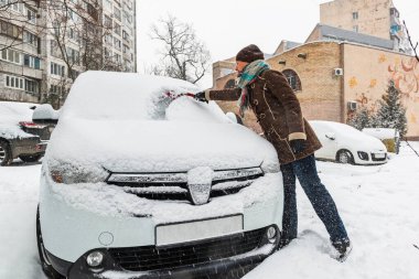 Kadın sürücü, kar yağarken arabasının ön camını temizliyor. Kış sürücüsü