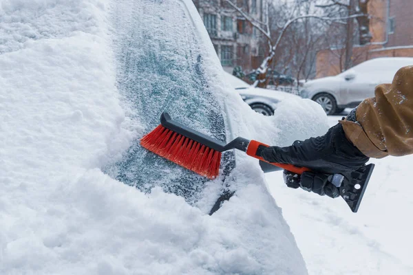 Kar arabasının ön camını fırçayla temizleyen bir el. Kışın araba kullanırken