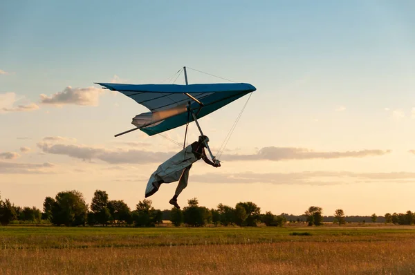 Learning to fly on a hang glider. Pilot prepares to land with his wing. Hang glider wing silhouette