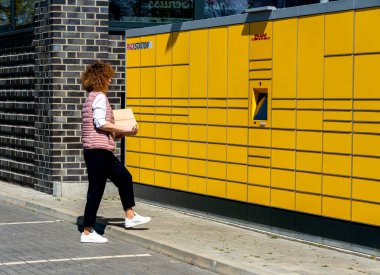 Bir kadın, DHL 'nin tipik sarı Alman paketleme istasyonlarından posta gönderir ve alır.