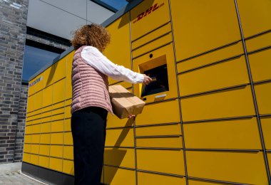 Bir kadın, DHL 'nin tipik sarı Alman paketleme istasyonlarından posta gönderir ve alır.