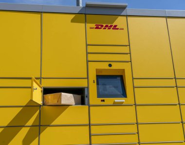 Bir kadın, DHL 'nin tipik sarı Alman paketleme istasyonlarından posta gönderir ve alır.