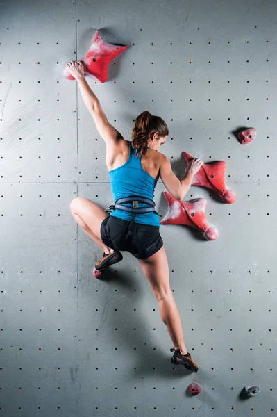 Young woman climbing up on practice wall in gym — Stock Photo, Image