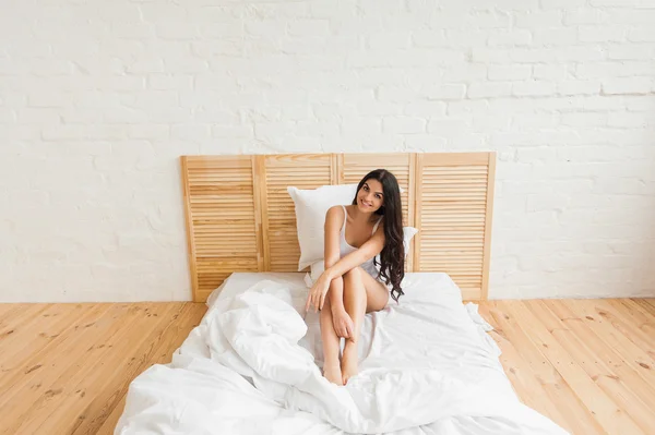 Lächelnde Frau sitzt in Unterwäsche auf dem weißen Bett — Stockfoto