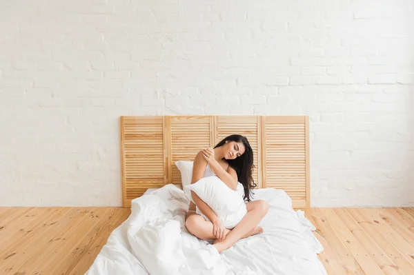 Mujer joven de la mañana con almohada sentada en la cama — Foto de Stock
