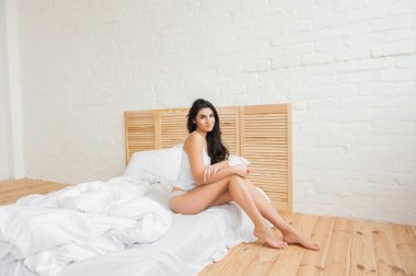 Sabah bir yatak üzerinde oturan gülümseyen genç kadın