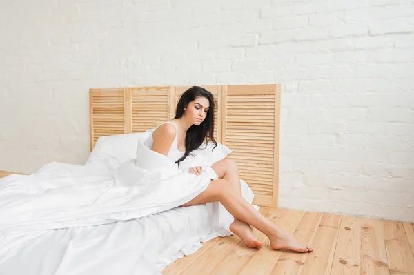 Mujer joven sexy serio sentado en el borde de la cama blanca — Foto de Stock