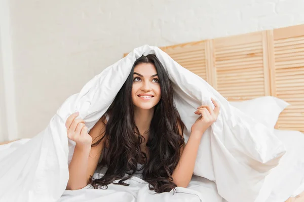 Mujer sonriente bajo manta mirando hacia arriba en su dormitorio — Foto de Stock