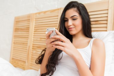 Gülümseyen kadın evde telefon ile yatakta