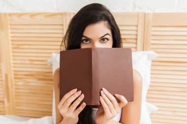 Güzel genç esmer kadın kendini bir kitap saklanıyor