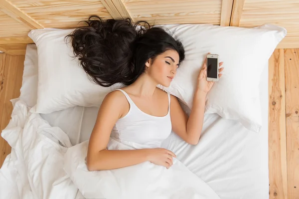 Woman sleeping in bed and holding mobile phone on pillow, — Stock Photo, Image