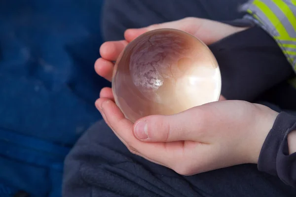 Shinig glass ball in child hands with landscape reflection