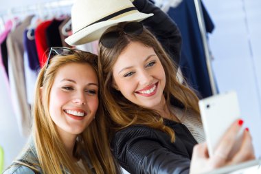 İki güzel genç kadın bir giysilerle cep telefonlarını kullanarak 