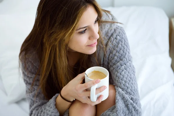 Schöne junge Frau trinkt Kaffee auf dem Bett. — Stockfoto