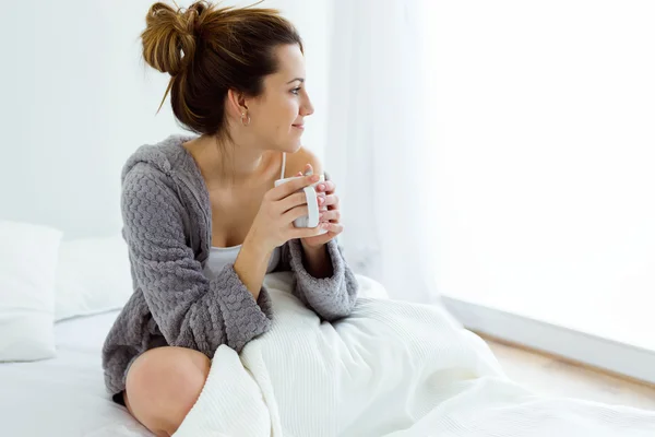 Vacker ung kvinna dricker kaffe på säng. — Stockfoto