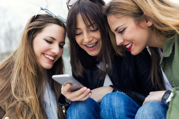 Tres mujeres jóvenes usando un teléfono móvil en la calle . — Foto de Stock