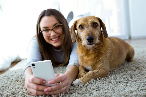 Mulher bonita com seu cão usando telefone celular em casa . — Fotografia de Stock