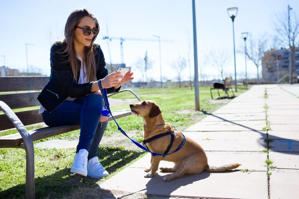 Frumoasa femeie tânără cu câinele ei folosind telefonul mobil . — Fotografie, imagine de stoc