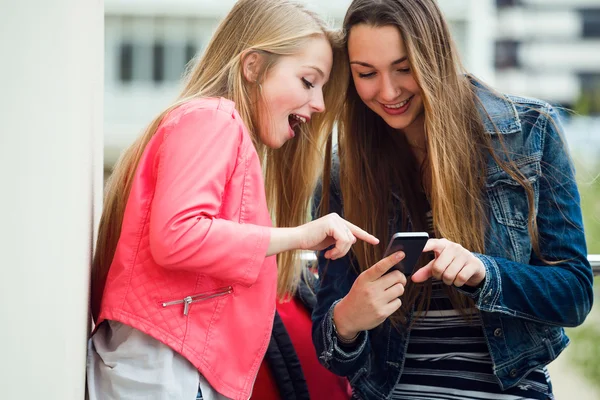 Dos hermosos estudiantes usando el teléfono móvil en la calle . — Foto de Stock