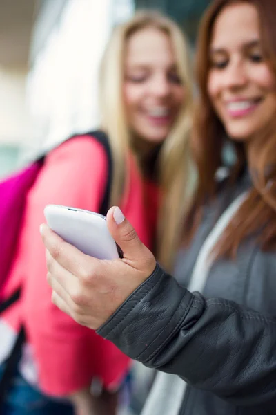 Dos hermosos estudiantes usando el teléfono móvil en la calle . —  Fotos de Stock