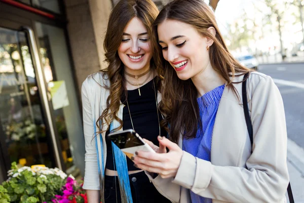 Duas belas jovens mulheres usando telefone celular na rua . — Fotografia de Stock