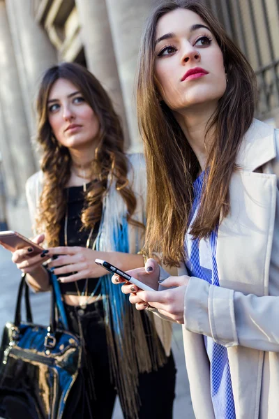 Duas belas jovens mulheres usando telefone celular na rua . — Fotografia de Stock