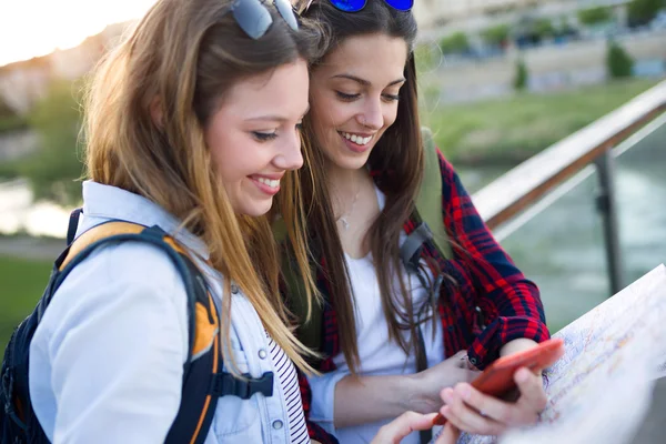 Två unga kvinnor turist använder sin mobiltelefon i staden. — Stockfoto