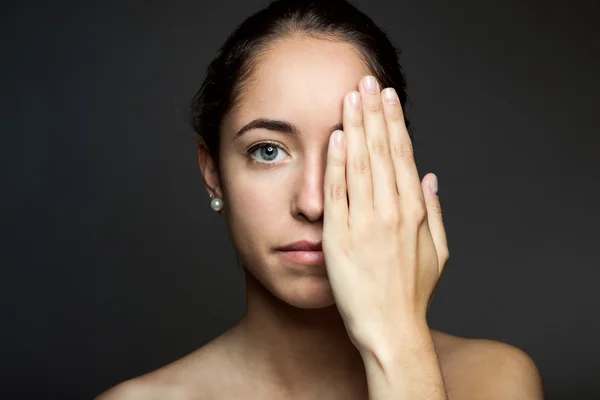 Jonge vrouw die betrekking hebben op de helft van haar gezicht met een hand. — Stockfoto