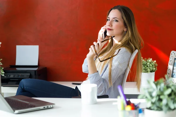 Belle jeune femme utilisant son téléphone portable dans le bureau . — Photo