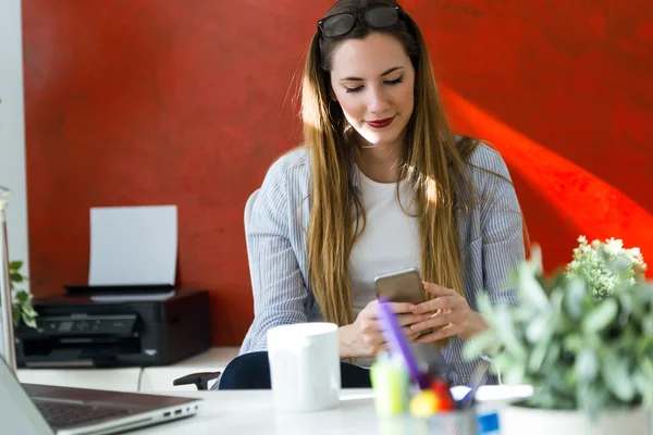 Hermosa mujer joven usando su teléfono móvil en la oficina . — Foto de Stock