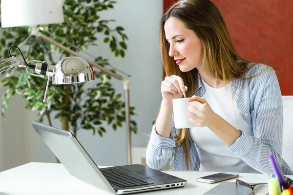 Mooie jonge vrouw met laptop in haar kantoor werken. — Stockfoto