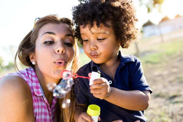 Hermosa madre joven con su hijo soplando burbujas de jabón en el parque . — Foto de Stock