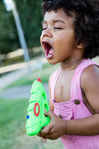 Afro-americano bebê brincando com arma de água no parque . — Fotografia de Stock