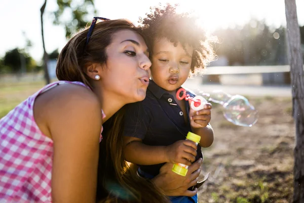 Güzel genç anne oğluyla parkta sabun köpüğü üfleme. — Stok fotoğraf