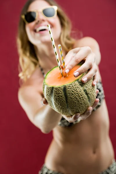 Piękna młoda kobieta w bikini picia sok z melona. Na czerwonym tle. — Zdjęcie stockowe
