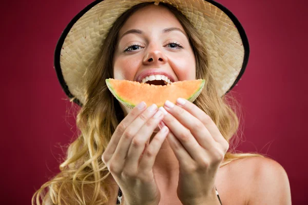 Beautiful young woman in bikini eating melon. Isolated on red. — Stock Photo, Image