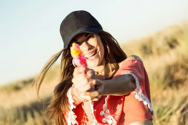 Mooie jonge vrouw, spelen met water gun automatische waterpistool op veld. — Stockfoto