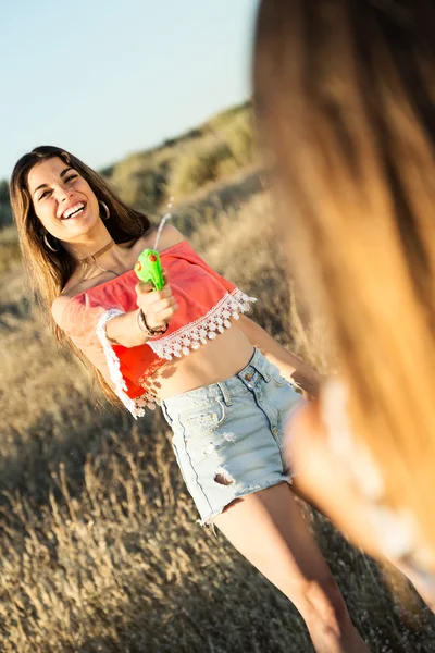 Beautiful young woman playing with water gun on field. — Stock Photo, Image
